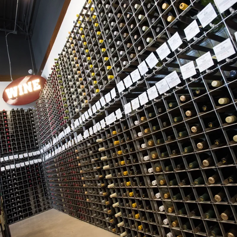 Floor-to-ceiling wine wall racks filling two full walls with rows of shelf talker cards beneath an illuminated wine sign at The PRIDE Stores