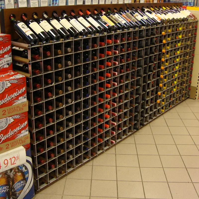 Single-sided free-standing wall wine racks with angled display bottles running along a retail perimeter wall at The PRIDE Stores