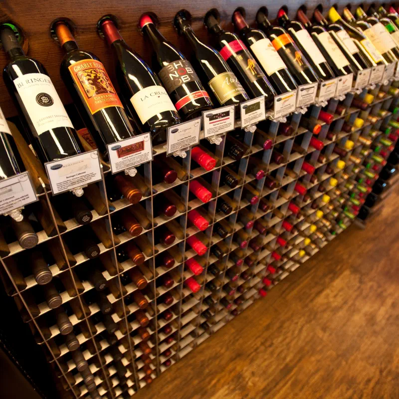 Angled wine rack display tops with shelf talker cards presenting feature bottles face-out above modular storage cells at The PRIDE Stores