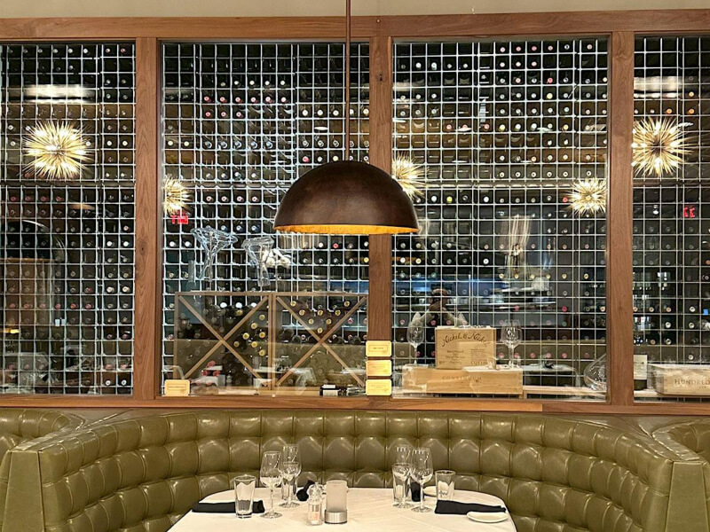 Guests dining beneath a floor-to-ceiling wine wall with aluminum framing and professional lighting at Sullivan's Steakhouse in Naperville, Illinois