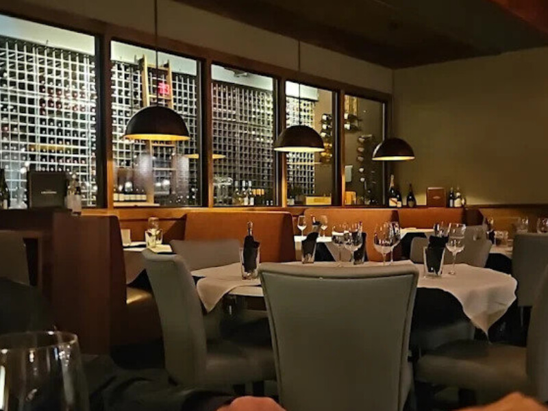 Wide view of fine dining room with floor-to-ceiling wine wall behind booth seating at Sullivan's Steakhouse in Wilmington, Delaware